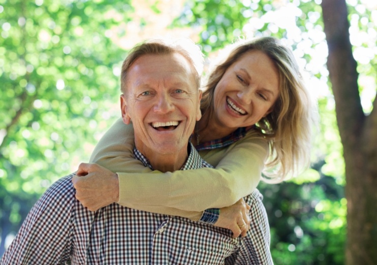 Smiling older couple hugging outdoors after visiting dental office in Naples