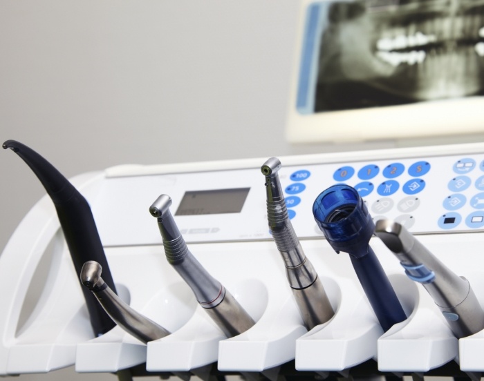 Row of dental instruments with an x ray of teeth on a screen in the background