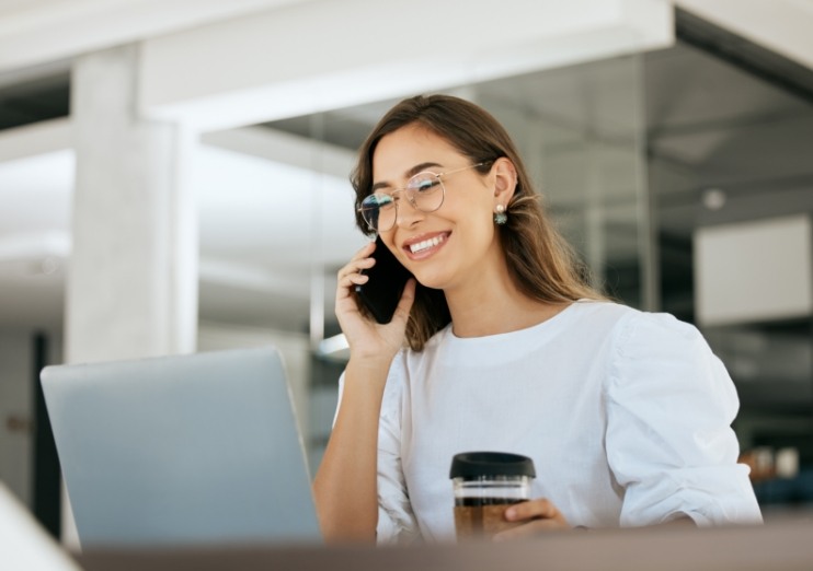 Woman at desk smiling while talking on the phone with Naples dental office