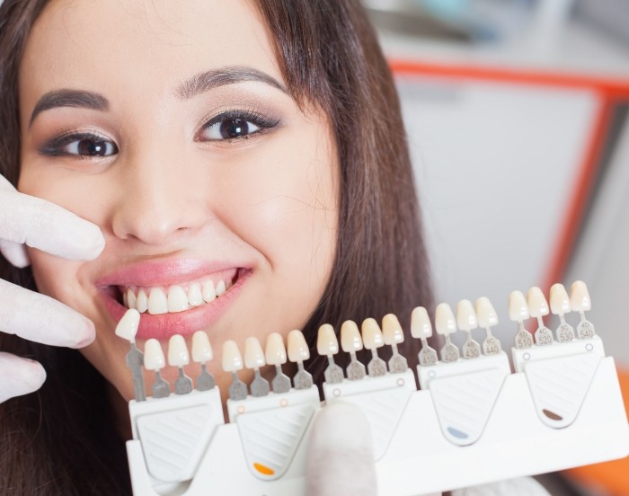 Dentist holding a veneer shade guide next to a smiling patients teeth