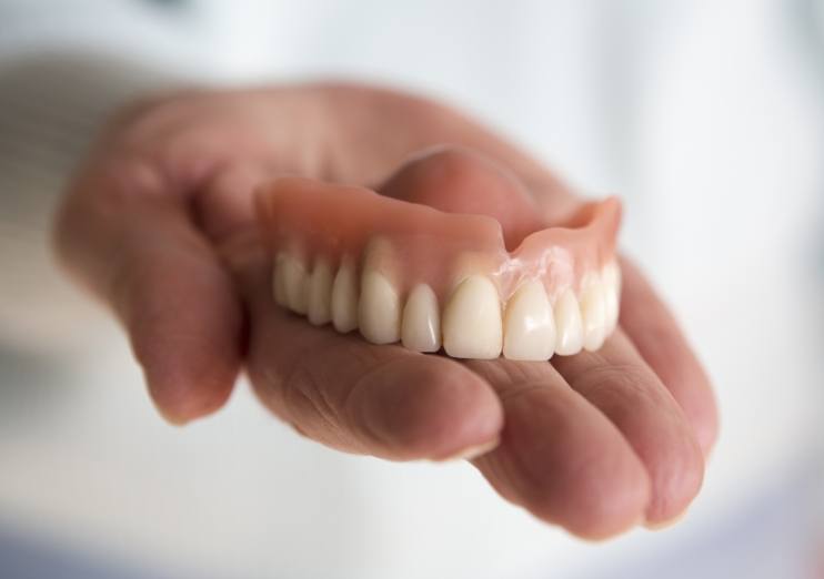 Hand holding a full upper denture in Naples