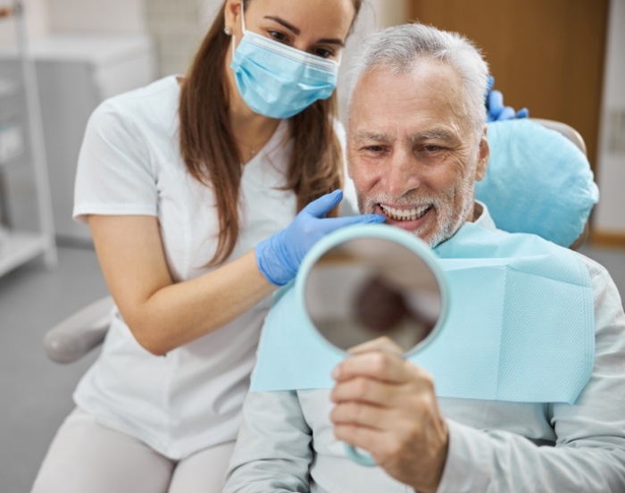 Senior dental patient looking at his new smile in a mirror