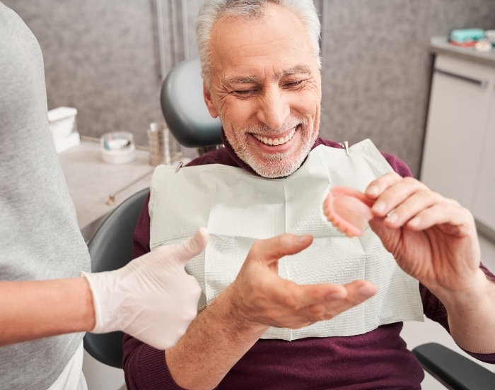 Senior man in dental chair smiling and holding a denture