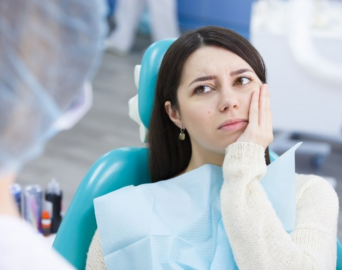 Woman in dental chair holding her cheek in pain