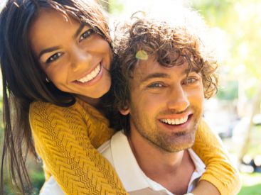 Smiling young woman hugging a smiling young man from behind