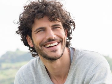 Man with curly brown hair smiling outdoors