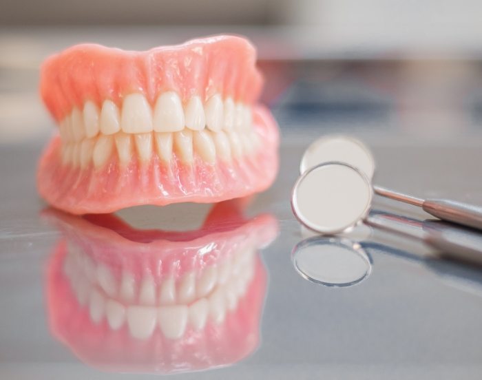 Set of full dentures on table next to two dental mirrors