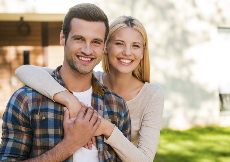 Young man and woman hugging outdoors and smiling after dental services in Naples