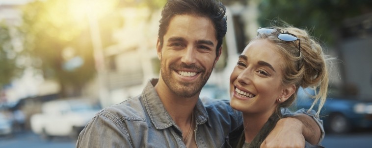 Young man and woman smiling while standing on city sidewalk