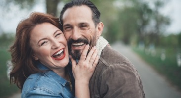 Man and woman laughing while hugging outside