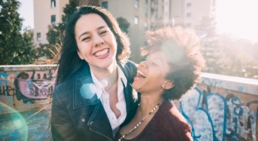 Two women laughing together outdoors on a sunny day