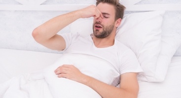 Man laying in bed and pinching the bridge of his nose