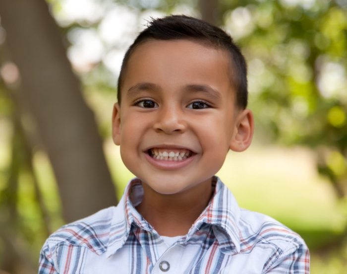 Young boy in striped collared shirt smiling outdoors