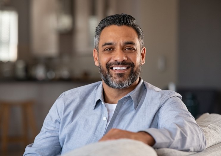 Smiling man sitting on couch and leaning over the back of the couch