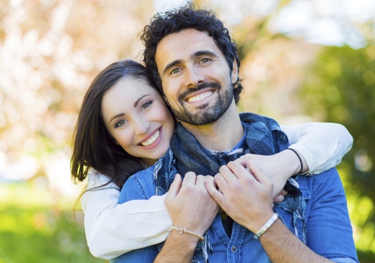 Smiling man and woman hugging outdoors after restorative dentistry in Naples