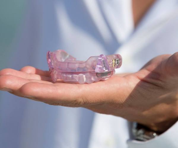 Hand holding a light purple splint to be worn over the teeth